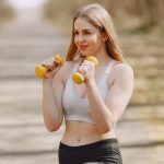Fit woman lifting dumbbells on a sunny day, embracing a healthy outdoor workout.