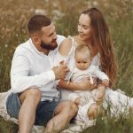A joyful couple with their baby sitting on a blanket in a sunny meadow, embracing the beauty of summer.